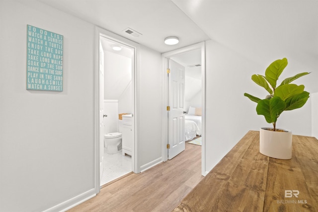 hallway with wood finished floors, baseboards, and visible vents