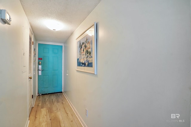 doorway with light wood-style floors, a textured ceiling, and baseboards