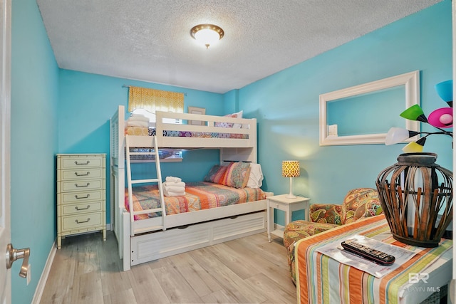 bedroom featuring light wood-type flooring, baseboards, and a textured ceiling