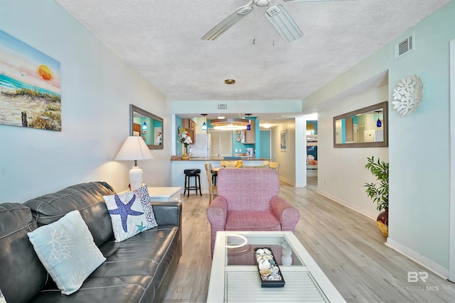 living area with light wood finished floors, baseboards, visible vents, and a textured ceiling