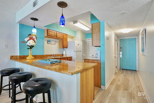 kitchen featuring a peninsula, freestanding refrigerator, a breakfast bar, and decorative light fixtures