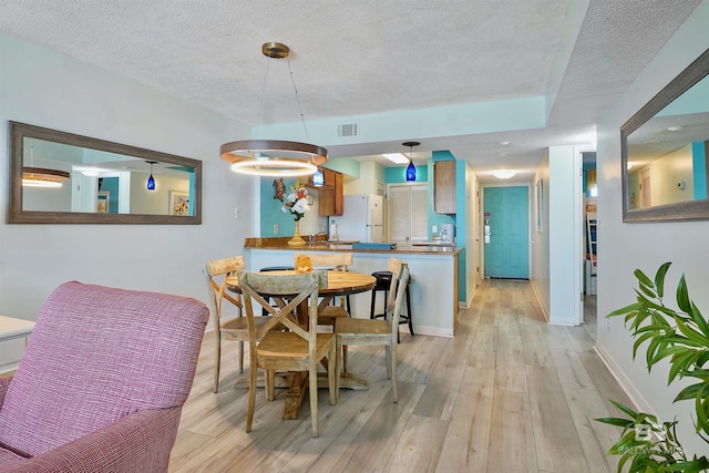 dining space with a textured ceiling, light wood finished floors, visible vents, and baseboards