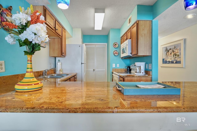 kitchen featuring a textured ceiling, white appliances, a sink, light countertops, and brown cabinets