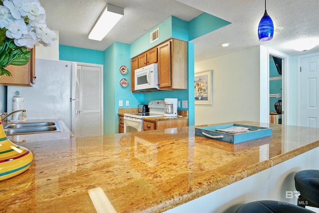 kitchen featuring white appliances, a sink, visible vents, brown cabinetry, and pendant lighting