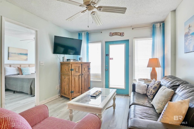 living area featuring light wood-type flooring, ceiling fan, baseboards, and a textured ceiling