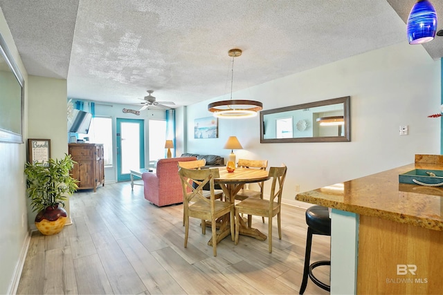 dining space featuring baseboards, ceiling fan, light wood-style flooring, and a textured ceiling