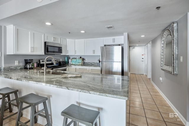 kitchen featuring light stone countertops, appliances with stainless steel finishes, white cabinets, and kitchen peninsula