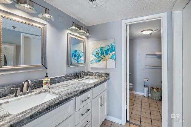 bathroom with tile patterned flooring, vanity, a textured ceiling, and toilet