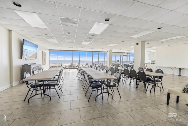 tiled dining area featuring floor to ceiling windows and a drop ceiling