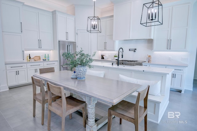 kitchen with white cabinetry, an island with sink, decorative backsplash, high quality fridge, and hanging light fixtures