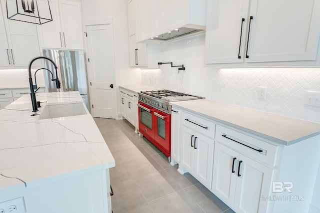 kitchen featuring white cabinetry, custom exhaust hood, light stone countertops, range, and sink