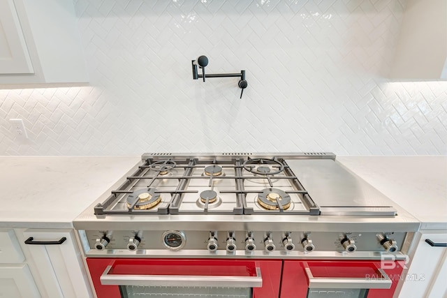 details featuring stainless steel gas stovetop, white cabinetry, backsplash, and light stone counters