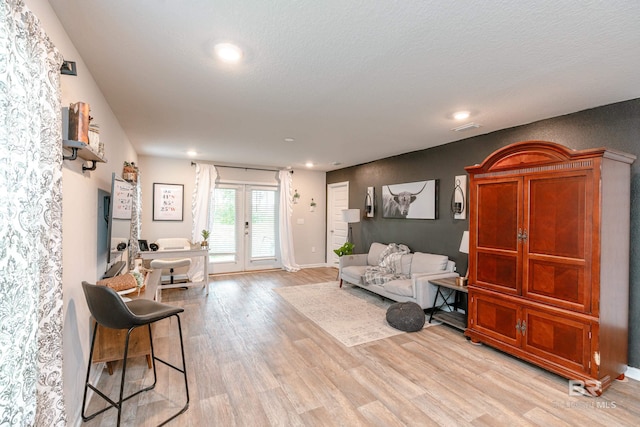 living room with french doors, a textured ceiling, and light hardwood / wood-style floors