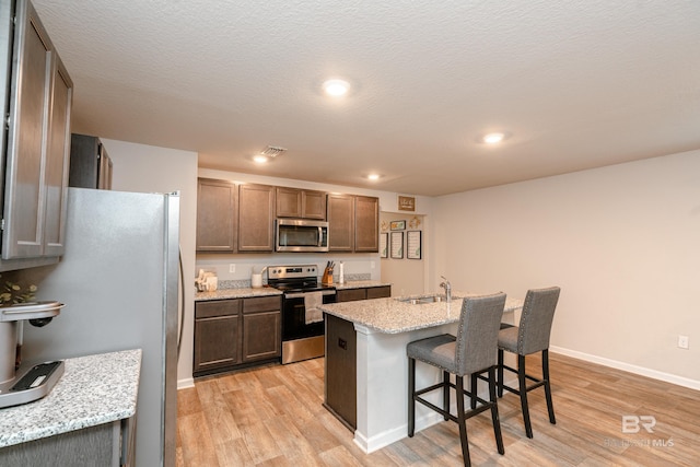 kitchen featuring a kitchen breakfast bar, a kitchen island with sink, stainless steel appliances, sink, and light wood-type flooring