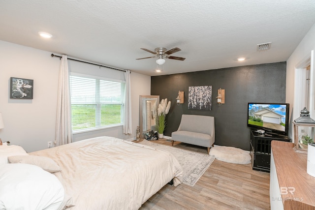 bedroom with light wood-type flooring, ceiling fan, and a textured ceiling