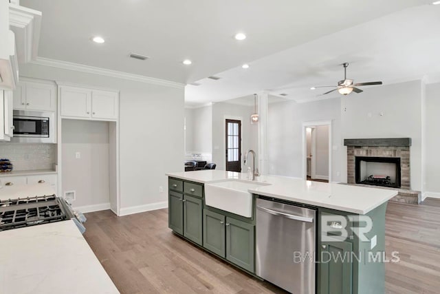 kitchen with stainless steel appliances, light wood-type flooring, green cabinetry, sink, and white cabinets