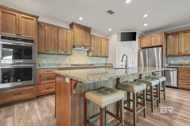 kitchen with visible vents, a breakfast bar area, appliances with stainless steel finishes, under cabinet range hood, and a sink