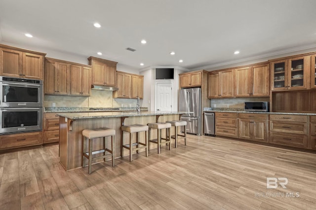 kitchen with under cabinet range hood, appliances with stainless steel finishes, brown cabinets, and a breakfast bar area