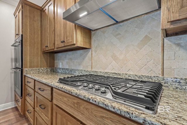 kitchen featuring stainless steel appliances, tasteful backsplash, brown cabinets, and exhaust hood