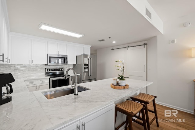 kitchen with sink, a breakfast bar, stainless steel appliances, light stone counters, and white cabinets