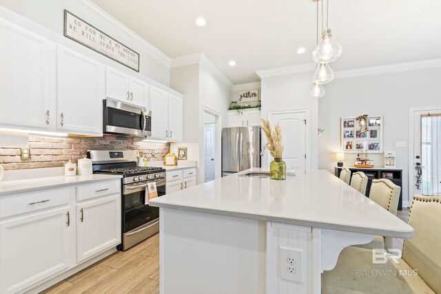 kitchen with white cabinets, decorative light fixtures, appliances with stainless steel finishes, a kitchen bar, and a kitchen island with sink