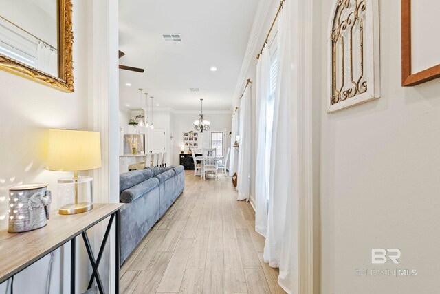 hall featuring ornamental molding, light wood-type flooring, and a chandelier