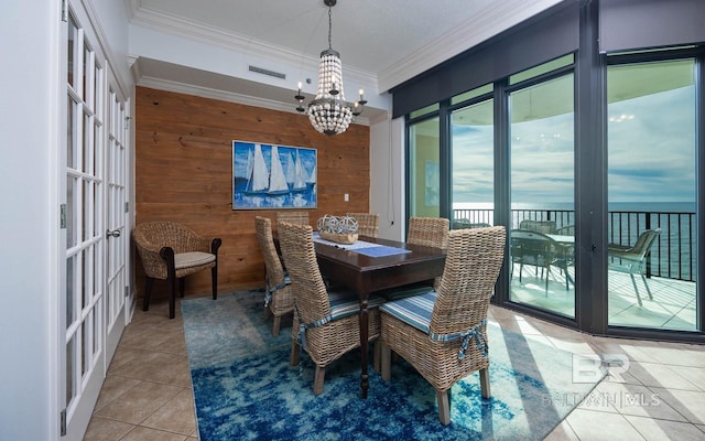 tiled dining area featuring french doors, crown molding, wooden walls, a water view, and a chandelier