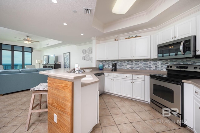 kitchen featuring kitchen peninsula, a breakfast bar, stainless steel appliances, a tray ceiling, and white cabinets