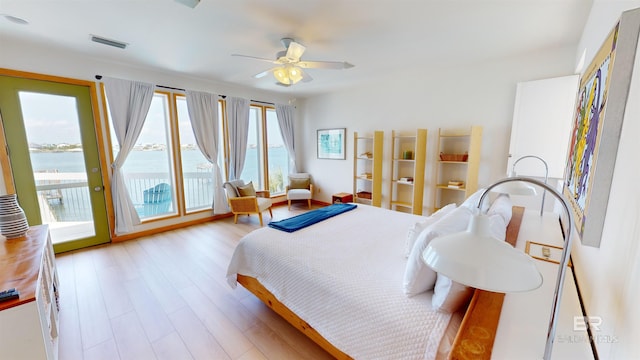 bedroom with access to outside, light wood-type flooring, a water view, and ceiling fan