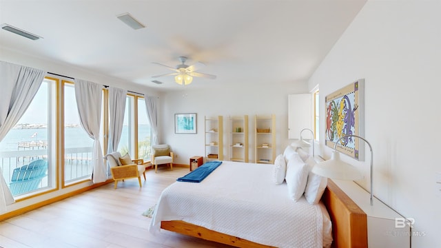 bedroom featuring multiple windows, light wood-type flooring, a water view, and ceiling fan