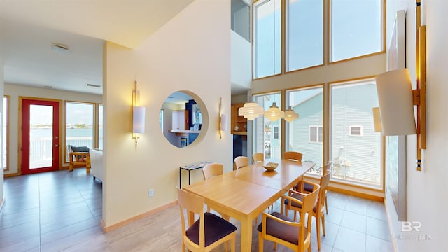 tiled dining space with a high ceiling, a healthy amount of sunlight, and a water view