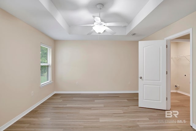 unfurnished bedroom with a raised ceiling, a walk in closet, light hardwood / wood-style flooring, ceiling fan, and a closet