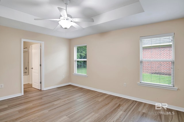 empty room featuring ceiling fan, light hardwood / wood-style floors, and a raised ceiling