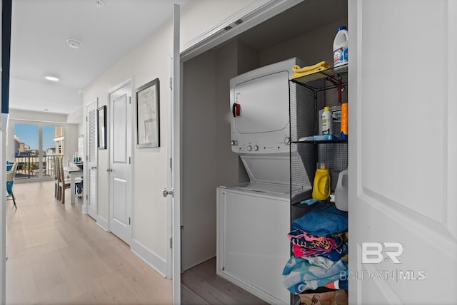 laundry area featuring stacked washing maching and dryer and light hardwood / wood-style flooring