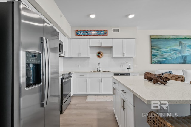 kitchen featuring light hardwood / wood-style flooring, stainless steel appliances, sink, light stone countertops, and white cabinets