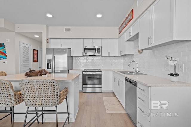 kitchen with a breakfast bar area, white cabinetry, stainless steel appliances, and light wood-type flooring