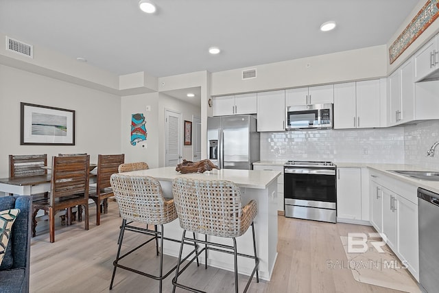 kitchen featuring appliances with stainless steel finishes, sink, light wood-type flooring, a center island, and white cabinetry