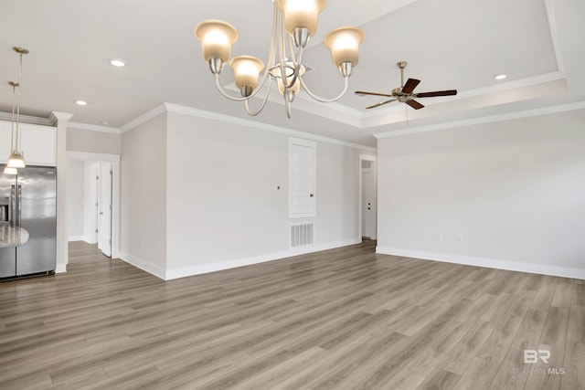 unfurnished living room with visible vents, ornamental molding, ceiling fan with notable chandelier, a tray ceiling, and light wood finished floors