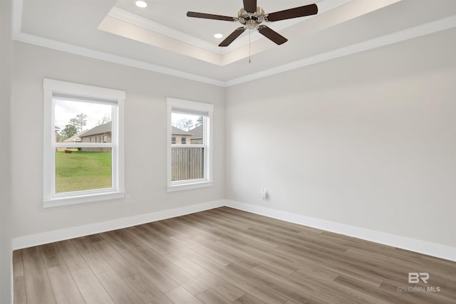 unfurnished room featuring a tray ceiling, baseboards, wood finished floors, and ornamental molding