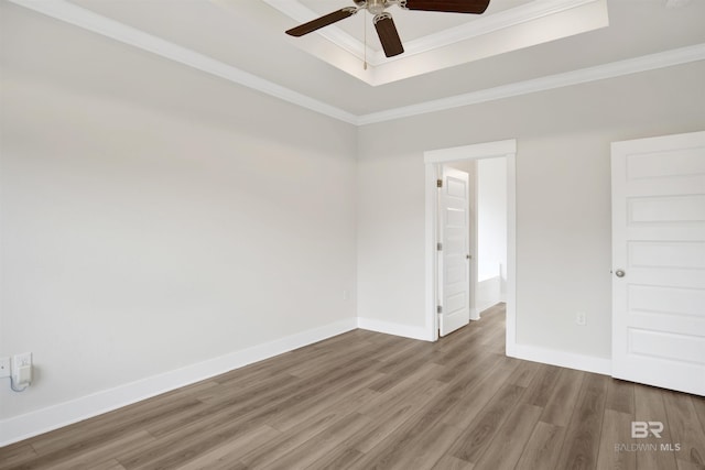 unfurnished room featuring a raised ceiling, ornamental molding, wood finished floors, baseboards, and ceiling fan