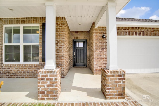 doorway to property featuring an attached garage, covered porch, and brick siding