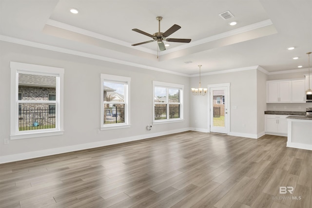 unfurnished living room with a tray ceiling, light wood-style floors, visible vents, and ornamental molding