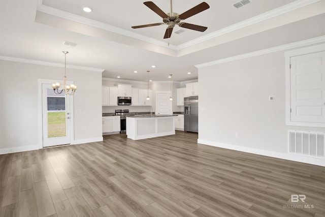 unfurnished living room featuring a tray ceiling, wood finished floors, ceiling fan with notable chandelier, and visible vents