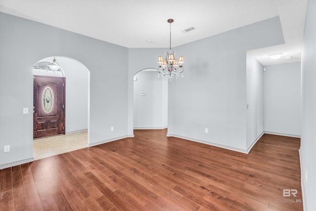 empty room featuring wood-type flooring and a chandelier