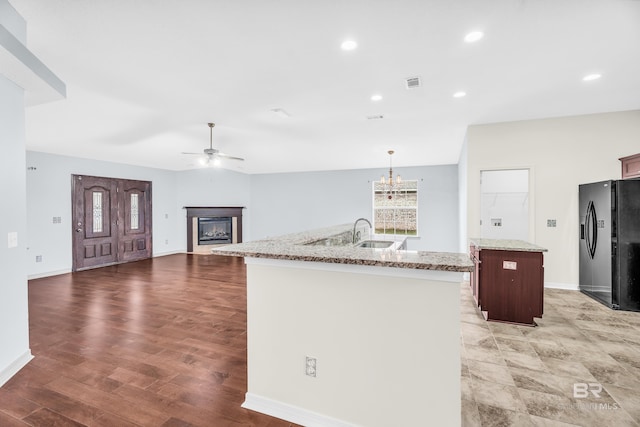 kitchen with pendant lighting, a center island with sink, sink, hardwood / wood-style flooring, and black fridge with ice dispenser