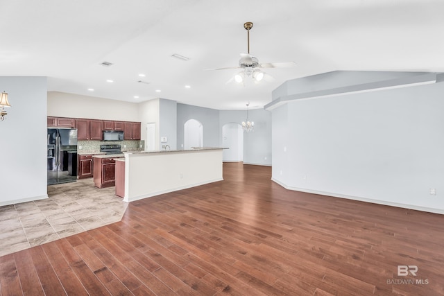 kitchen featuring lofted ceiling, black appliances, ceiling fan with notable chandelier, hardwood / wood-style flooring, and decorative backsplash