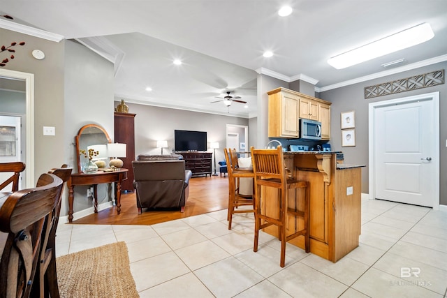 kitchen with light tile patterned floors, light brown cabinetry, ornamental molding, and stainless steel microwave