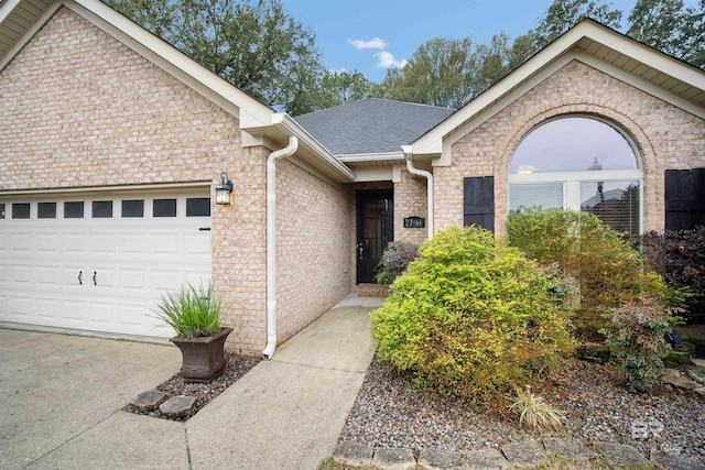 ranch-style house with concrete driveway, roof with shingles, brick siding, and an attached garage