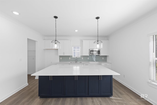 4645 Casablanca Dr, Orange Beach, AL 36561 - kitchen featuring stainless steel microwave, a sink, white cabinetry, wood finished floors, and ornamental molding