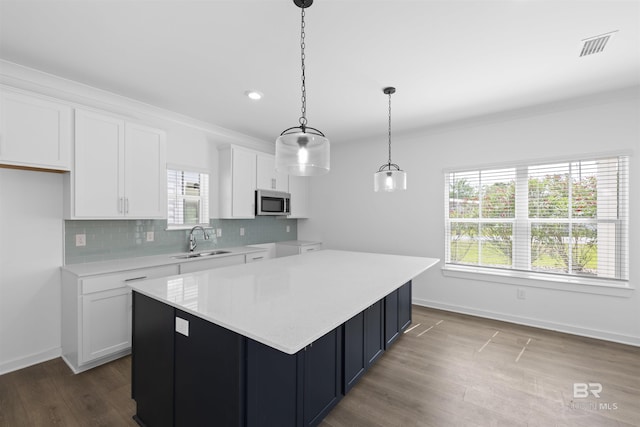 4645 Casablanca Dr, Orange Beach, AL 36561 - kitchen with stainless steel microwave, a sink, white cabinets, light countertops, and decorative backsplash